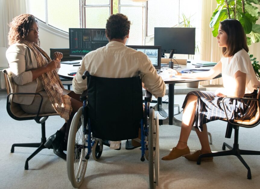 Photo of male wheelchair user in office round desk with two women