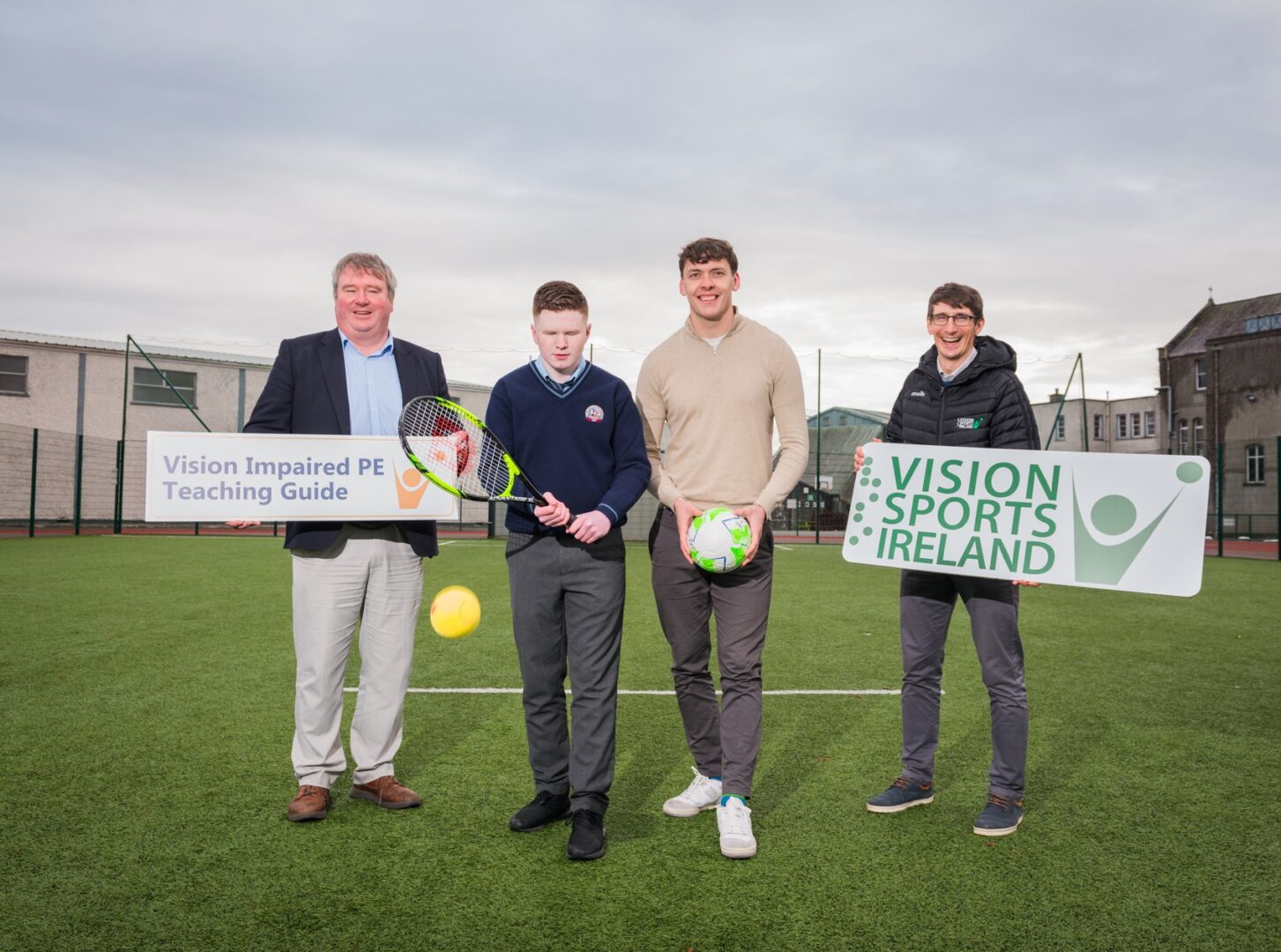 Photo of Senator Martin Conway, Kerry footballer David Clifford and two others standing on playing pitch with signs saying Vision Impaired PE Teaching Guide and Vision Sports Ireland.